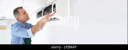 Electrician with screwdriver repairing air conditioner indoors, space for text. Banner design Stock Photo