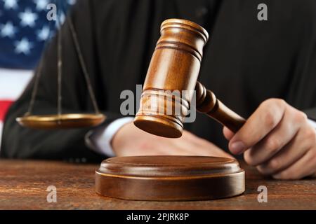 Judge with gavel at wooden table near flag of United States, closeup Stock Photo