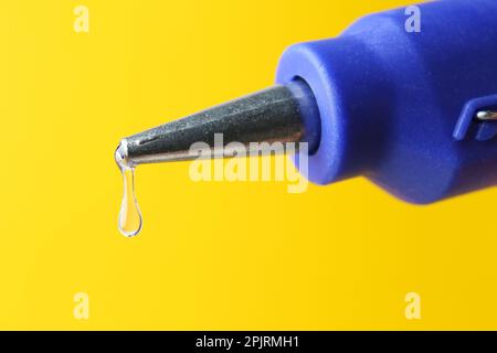 Dripping hot glue from gun on yellow background, closeup Stock Photo