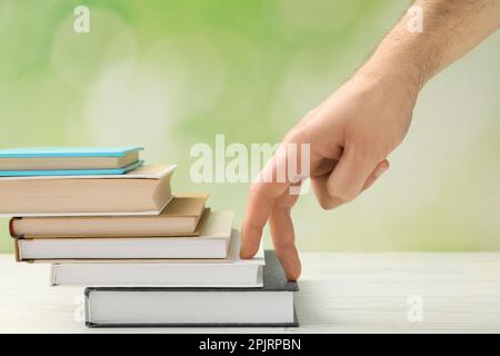 Man climbing up stairs of books with fingers on white wooden table against blurred background, closeup Stock Photo