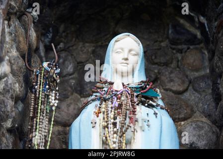 Nov 21, 2023, Puente Nacional, Santander, Colombia: Statue of the Virgin located outdoors with many rosaries hanging and protected in a stone niche. C Stock Photo