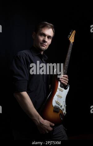 Studio low key portrait of caucasian man with electric guitar with dark lighting Stock Photo