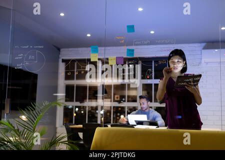 Diverse business people working and brainstorming on glass wall, late at office Stock Photo
