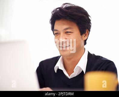 Tackling his work with a can-do attitude. a handsome asian businessman smiling while working on his laptop in the office. Stock Photo