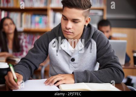 Focused on his work. a handsome young student working diligently in his classroom. Stock Photo