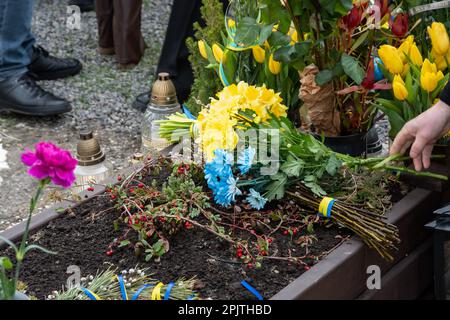 Flowers seen laid on the grave of a fallen soldier in Lviv. Yurii Ruf was a Lviv writer, public figure, patriot of Ukraine and a well-known person in Lviv and Ukraine. He organized many events, a festival, etc. When the war began, he went to the front as a volunteer and was killed during a combat mission in Luhansk region on April 1, 2022. The event in the photos is the commemoration of Yuriy in the church and on the field of honorable burials at the Lychakivskyi cemetery in Lviv on the first anniversary of his death. Relatives, friends and residents of the city who remember his contribution t Stock Photo