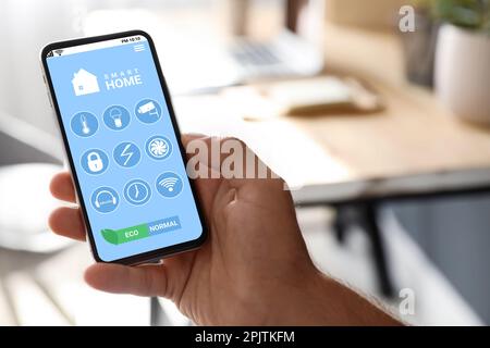 Man using Smart Home app on mobile phone indoors, closeup Stock Photo