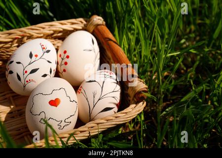 Wicker basket with decorated Easter eggs in green grass outdoors, closeup. Space for text Stock Photo