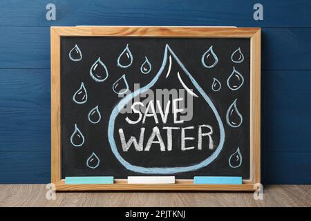 Blackboard with words Save Water and pieces of chalk on wooden table Stock Photo
