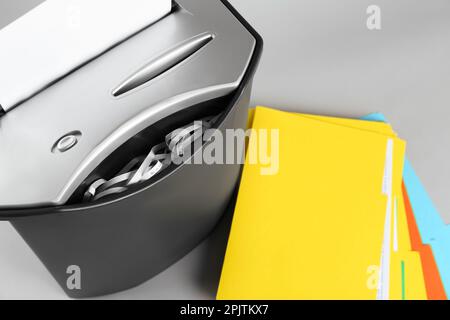 Shredder with sheet of paper and colorful folders on grey background, above view. Space for text Stock Photo