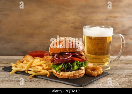 Tasty burger, French fries, fried onion rings and beer on wooden table. Fast food Stock Photo