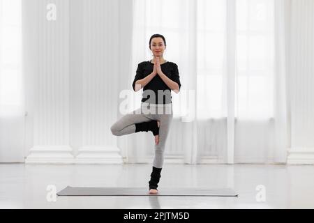Pretty young woman doing vrikshasana on a mat on the floor in her spacious  studio. Concept of benefits for the formation of correct posture heals  Stock Photo - Alamy