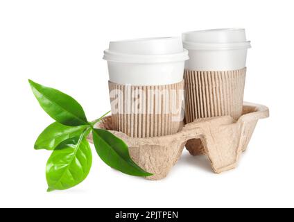 Takeaway paper coffee cups with sleeves in cardboard holder and green leaves on white background. Eco friendly lifestyle Stock Photo