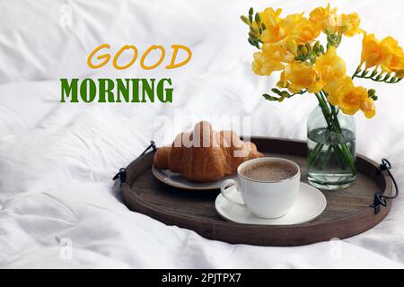 Good Morning! Cup of coffee, croissant and flowers on bed Stock Photo