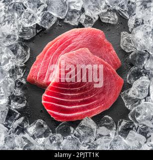 Chilled tuna steak on stone black slate serving plate and ice cubes arranged as a frame. Top view. Stock Photo