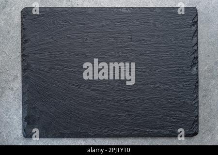 Empty natural stone black slate serving plate on light grey background. Flat lay. Stock Photo