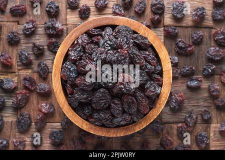 dried grapes, dark raisins in bowl on wooden table background. Stock Photo