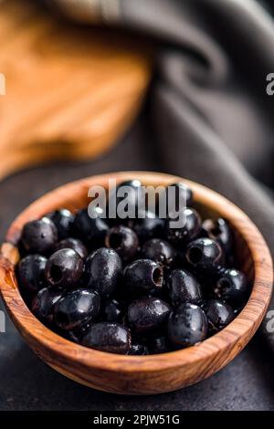 Pitted black olives in wooden bowl on the kitchen table. Stock Photo