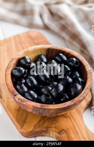 Pitted black olives in wooden bowl on the kitchen table. Stock Photo