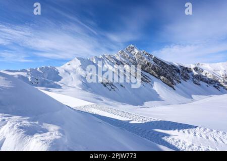 A scenic winter landscape shows a snow-covered field in the foreground with majestic mountain peaks in the background Stock Photo