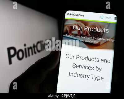 Person holding smartphone with webpage of US healthcare software company PointClickCare on screen with logo. Focus on center of phone display. Stock Photo