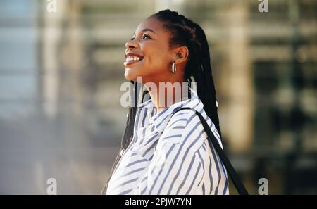 Happy young businesswoman smiling and looking away while walking to work in the city. Sideview of a cheerful young black business woman commuting to h Stock Photo