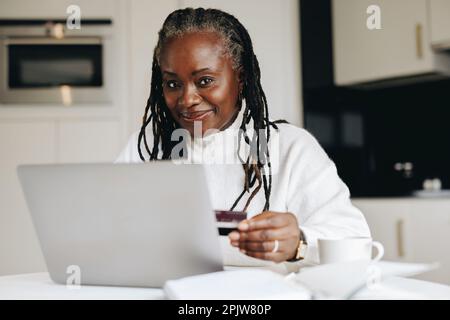 Mature woman looking at the camera while making an online payment with a credit card. Ethnic senior woman doing some online shopping for her freelance Stock Photo