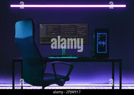 Home office programmer workplace with professional coding setup on desktop. Modern powerful PC and display with programming code in coder studio in neon lights. Stock Photo