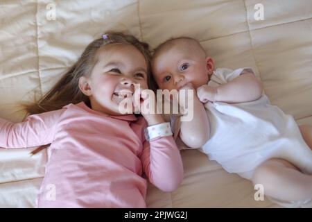 Little girl lying on bed next to her baby brother Stock Photo