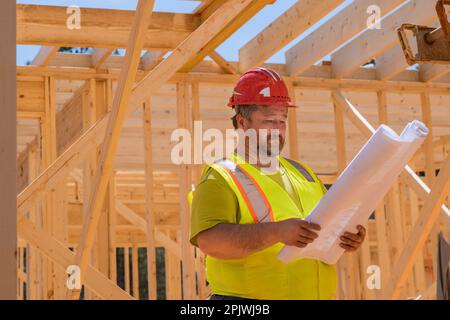 During construction on construction site construction engineer checks quality of wooden frame work using architecture blueprint plan Stock Photo