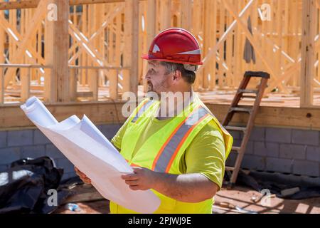Construction engineer checks quality of performed wooden frame using an architecture blueprint plan during work on construction site Stock Photo