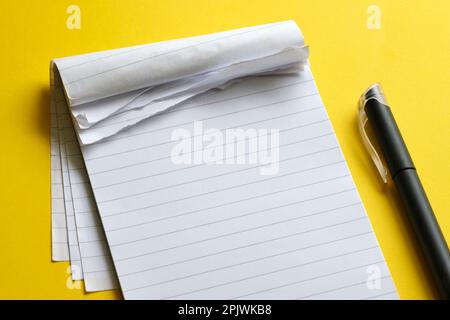 Top view of blank open notebook with torn pages. Page with lines and black minimalistic fineliner pen on yellow background with copy space. Stock Photo