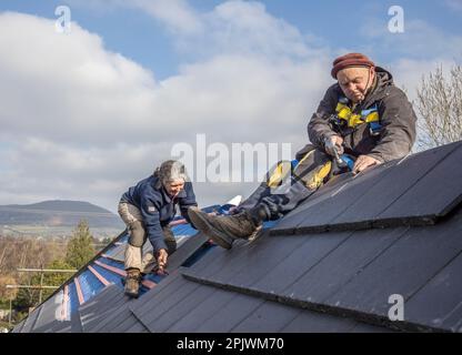 Roofer and assistant working on the ridge fixing new replacement tiles on a house, Llanfoist, Wales, UK Stock Photo