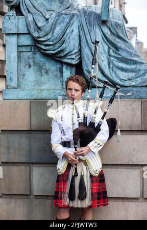 -Edinburgh,Scotland October 16, 2015  Scottish bagpiper dressed in traditional red and black tartan dress stand before stone wall. Edinburgh, the most Stock Photo