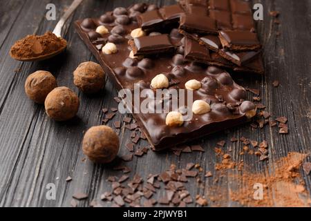 Handmade chocolate with hazelnuts, dark chocolate pieces, cocoa in a vintage spoon, chocolate truffles on a dark wooden background. Chocolate variety Stock Photo