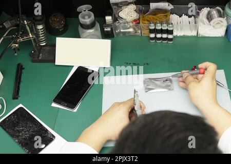 A mobile phone repair technician working in his small cubicle Stock Photo