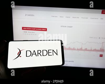 Person holding mobile phone with logo of US gastronomy company Darden Restaurants Inc. on screen in front of web page. Focus on phone display. Stock Photo