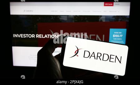 Person holding cellphone with logo of US gastronomy company Darden Restaurants Inc. on screen in front of webpage. Focus on phone display. Stock Photo