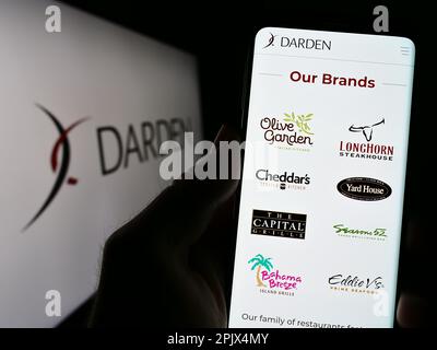 Person holding mobile phone with website of US gastronomy company Darden Restaurants Inc. on screen with logo. Focus on center of phone display. Stock Photo