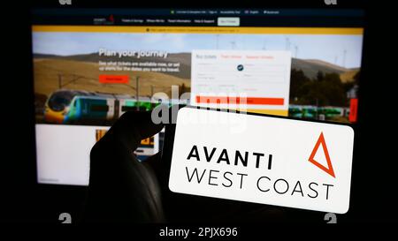 Person holding mobile phone with logo of British train company Avanti West Coast on screen in front of business web page. Focus on phone display. Stock Photo