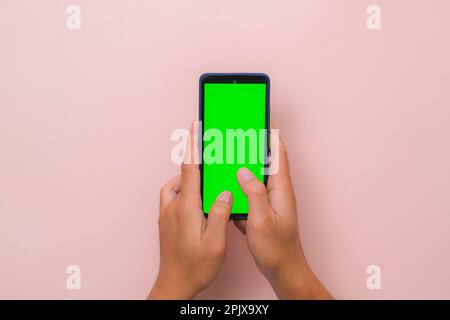 Human hand using mobile smartphone with mockup green screen on pink background. Male hand tapping and pinch to zoom in or zoom out on blank digital sc Stock Photo