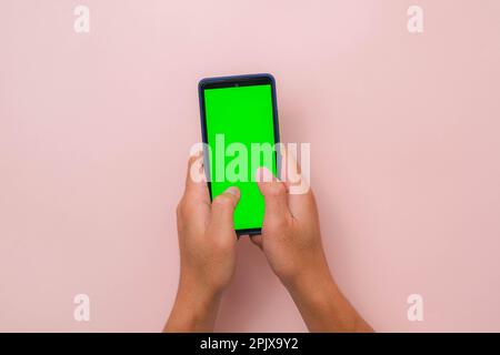 Human hand using mobile smartphone with mockup green screen on pink background. Male hand tapping and pinch to zoom in or zoom out on blank digital sc Stock Photo
