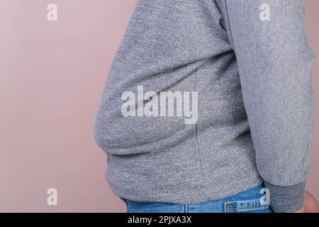 Fat woman hand holding excessive belly fat isolated on pink background. Overweight fatty belly of woman. Female diet and body health care concept Stock Photo