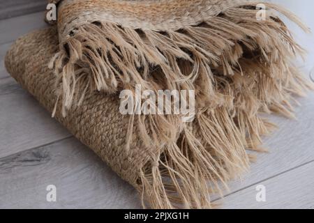 Fringed woven jute carpet rug , woven jute rug with fringe folded on the parquet in the bedroom. Jute carpet concept idea photo. Stock Photo