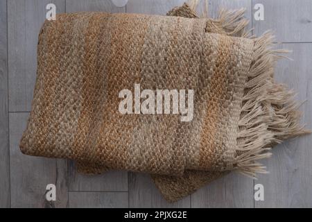 Fringed jute rug, top view of folded modern natural braided jute rug with fringe on the parquet in the bedroom. Jute carpet concept idea photo. Stock Photo