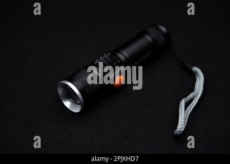 Metal black flashlight on a black background. Pocket flashlight. Stock Photo