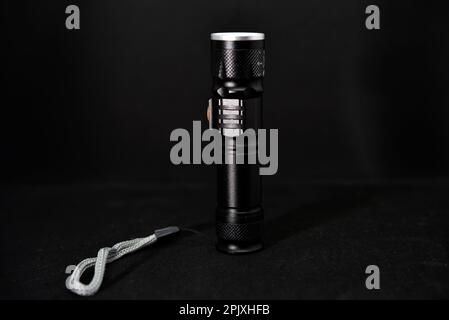 Metal black flashlight on a black background. Pocket flashlight. Stock Photo