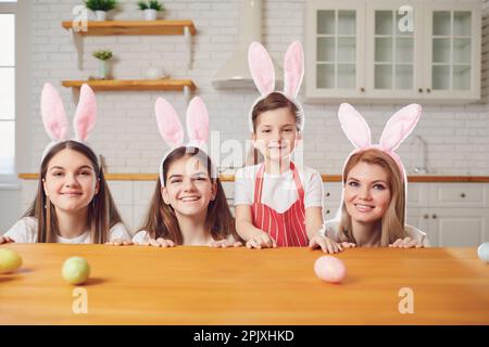 Happy easter. Mother and daughters with rabbit ears decorate Easter eggs at a table in kitchen. Stock Photo