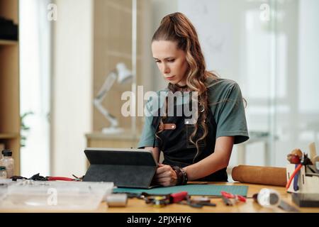 Leather worker checking e-mails and orders from clients on tablet computer Stock Photo