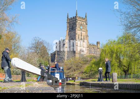 Kidderminster, UK. 4th April, 2023. UK weather: plenty of spring sunshine and blue skies makes for a perfect day on the British waterways. A family and friends are all aboard their holiday narrowboat as they pass through a lock on the Staffordshire and Worcestershire canal in Kidderminster with the beautiful St Mary's Parish Church looking splendid behind. Credit: Lee Hudson/Alamy Live News Stock Photo